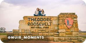 A woman and two children sitting on top of a large stone sign for Theodore Roosevelt National Park, with overlay text that reads: @muir_moments