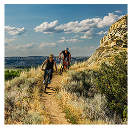 Two people riding bikes on a grassy, hilly trail