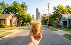 A hand holds an iced drink with a backdrop of the Austin skyline