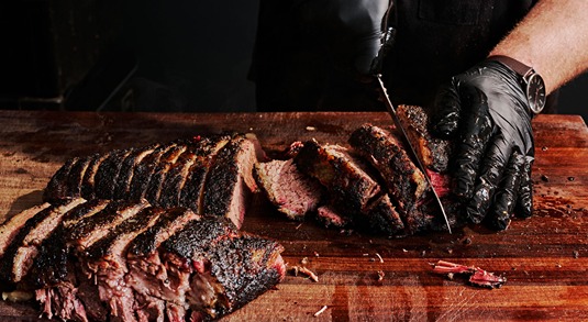 A pair of hands wearing black gloves slices freshly smoked beef brisket in Austin, Texas