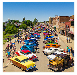Aerial view of colorful classic cars lined up on a small-town street with crowds of people around them