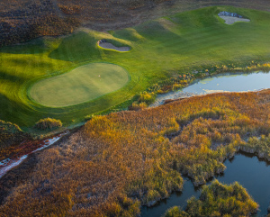 Aerial view of a golf course next to a landscape of red and orange foliage