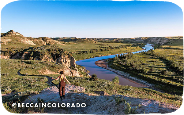 View of a woman from behind walking in a rocky landscape with a river in the background, with overlay text that reads: @beccaincolorado