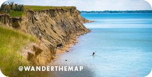 Aerial view of light blue water bordering a cliff, with overlay text that reads: @wanderthemap