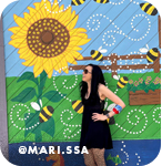Woman posing in front of a mural of sunflowers and bees, with overlay text that reads: @mari.ssa