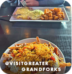 Two full dishes of food at a restaurant table, with overlay text that reads: @visitgreatergrandforks