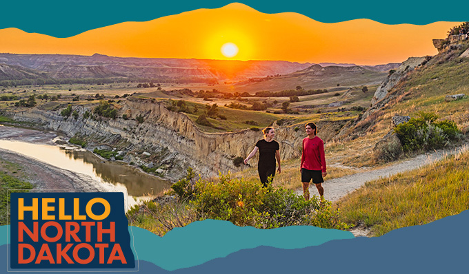Two people walking on a trail surrounded by beautiful hills and an orange sunset in the background, with overlay text that reads: Hello North Dakota