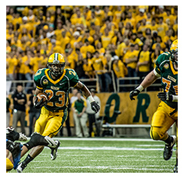 Football team in North Dakota playing a game with a crowd dressed in yellow shirts in the background
