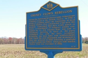Deep blue and gold historical marker of Cheney Clow's Rebellion stands alone in a field	