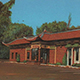 Building with a red tile roof and curved eaves, upturned roof corners that were adorned with dragons at the ridge line. There is a centrally placed glass vestibule with side door entries and elongated fixed windows highlighted by wide surrounds topped with green overhanging hooded eaves. 	