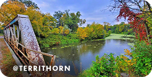 A metal bridge over a river lined with trees of green, yellow and red leaves, with overlay text that reads: @territhorn