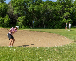 A golfer hitting a ball out of a sand trap on a golf course in North Dakota