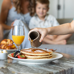 At a breakfast dining table, a person pours syrup onto a stack of pancakes at Omni Barton Creek Resort & Spa