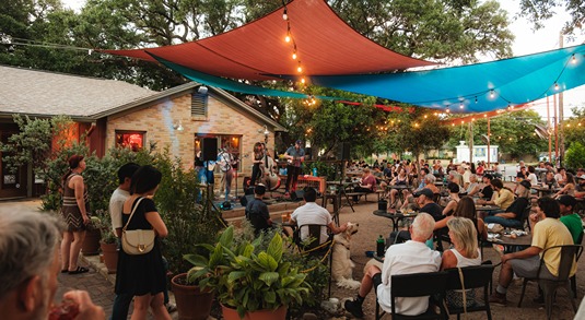 People listen to a band while sitting under colorful shade sails on the patio of Radio Coffee & Beer in Austin, Texas 