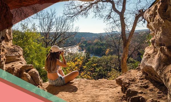 A woman aims her camera to take a photo while sitting on a scenic overlook at the Barton Creek Greenbelt in Austin, Texas