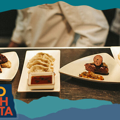 Wood table at a restaurant with dishes like sausage and potstickers on white plates, with overlay text that reads: HELLO NORTH DAKOTA