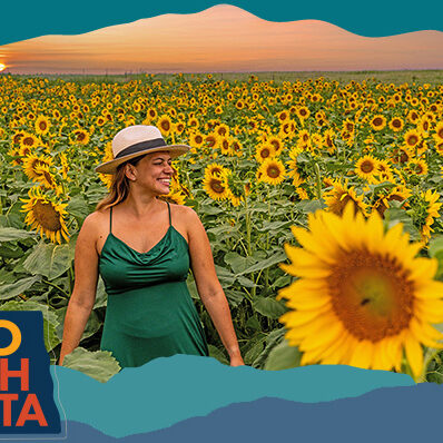 Smiling woman wearing a hat and a green dress walking through a large field of sunflowers with a sunset in the background, with overlay text that reads: Hello North Dakota