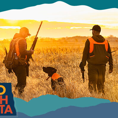 View from behind of two men standing in a field with a dog, holding hunting rifles with sunset in the background, with overlay text that reads: Hello North Dakota