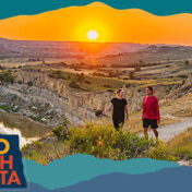 Two people walking on a trail surrounded by beautiful hills and an orange sunset in the background, with overlay text that reads: Hello North Dakota