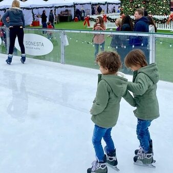 Two children hold on to each other while ice skating outdoors at skating at the Hill Country Galleria