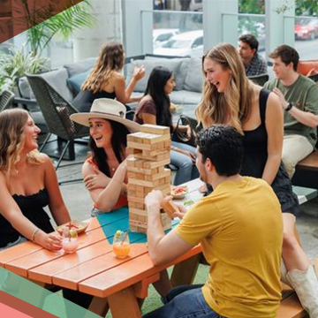 Groups of people socialize at picnic tables outdoors at Upstairs at Caroline, a rooftop bar and restaurant in Austin, Texas