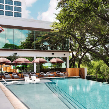A view of the main pool surrounded by lounge chairs under umbrellas at The LINE Austin hotel